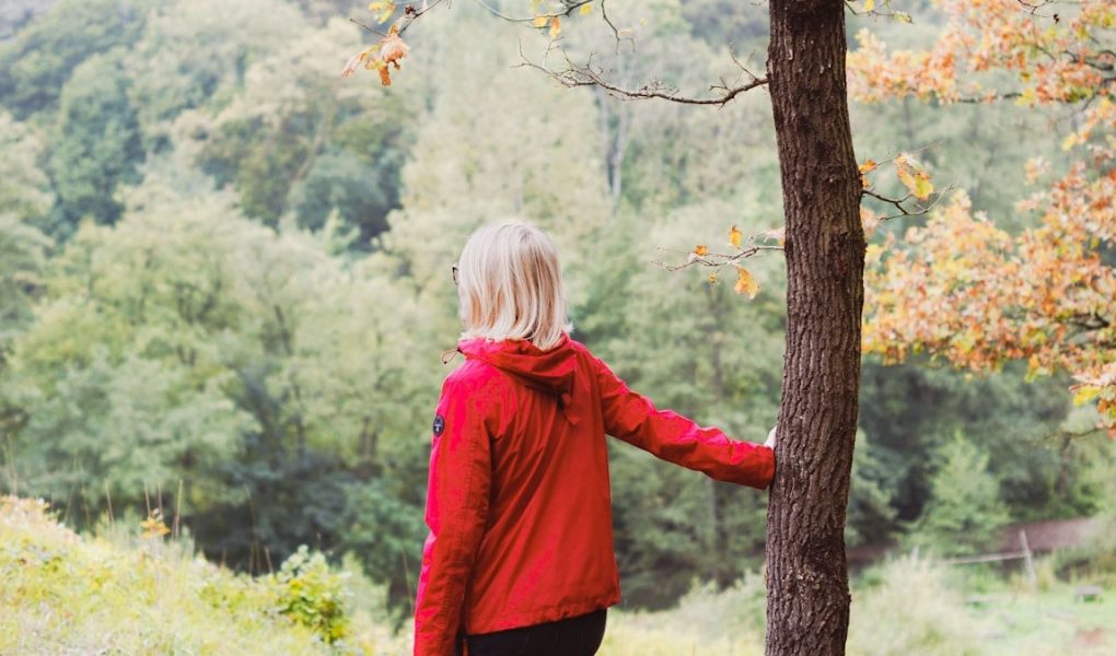 girl in red jacket standing beside brown tree during daytime