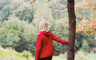 girl in red jacket standing beside brown tree during daytime