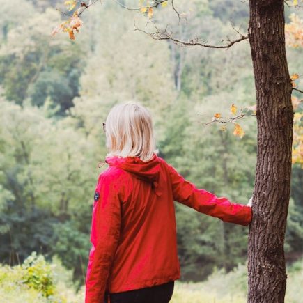 girl in red jacket standing beside brown tree during daytime