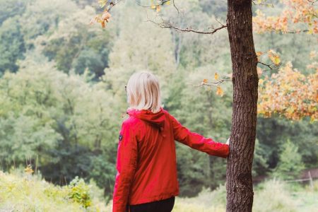 girl in red jacket standing beside brown tree during daytime