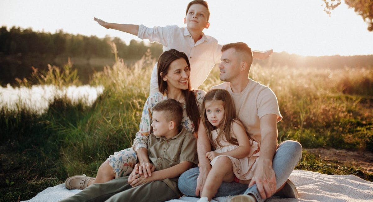 A family of five enjoying a serene picnic in a sunlit meadow during sunset.