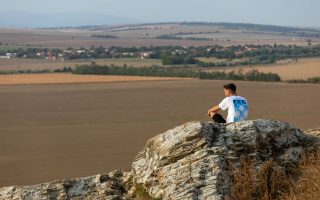 A man sits on a rock overlooking the vast countryside in a serene outdoor setting.