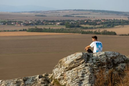 A man sits on a rock overlooking the vast countryside in a serene outdoor setting.